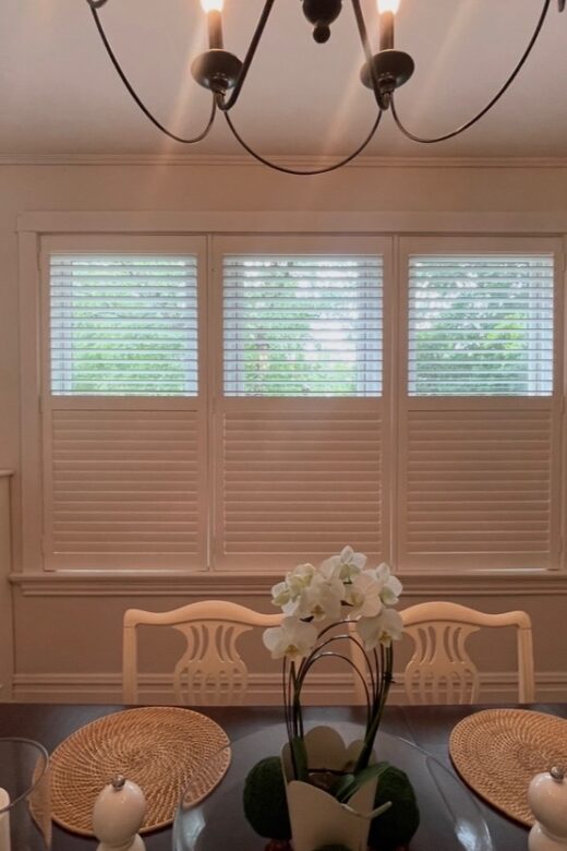Custom plantation shutters installed across three dining room windows with adjustable louvers.